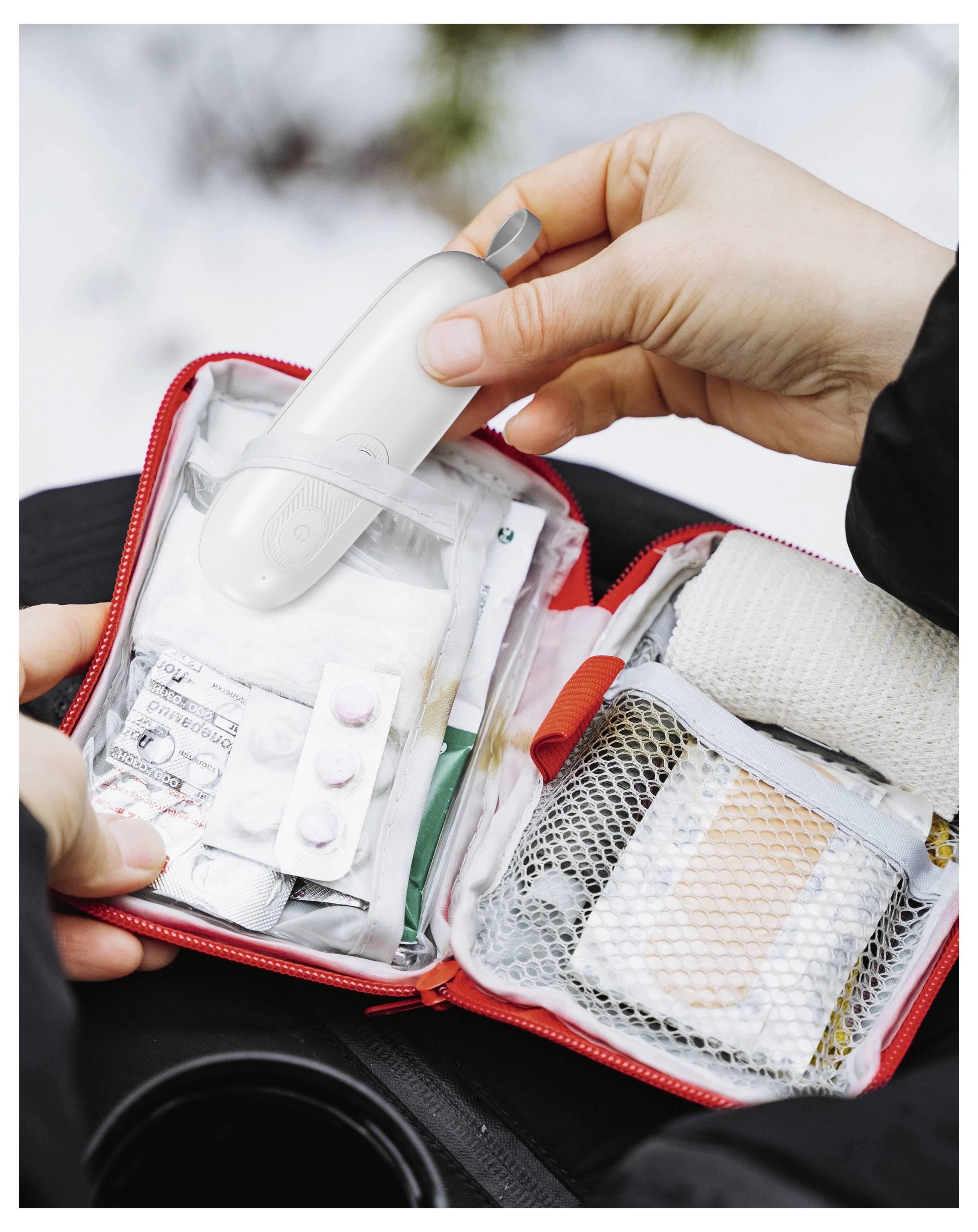 Eine Person öffnet einen roten Erste-Hilfe-Kasten, der Medikamente, Gaze und ein weißes medizinisches Gerät enthält, und zeigt damit Vorbereitung auf Notfälle.