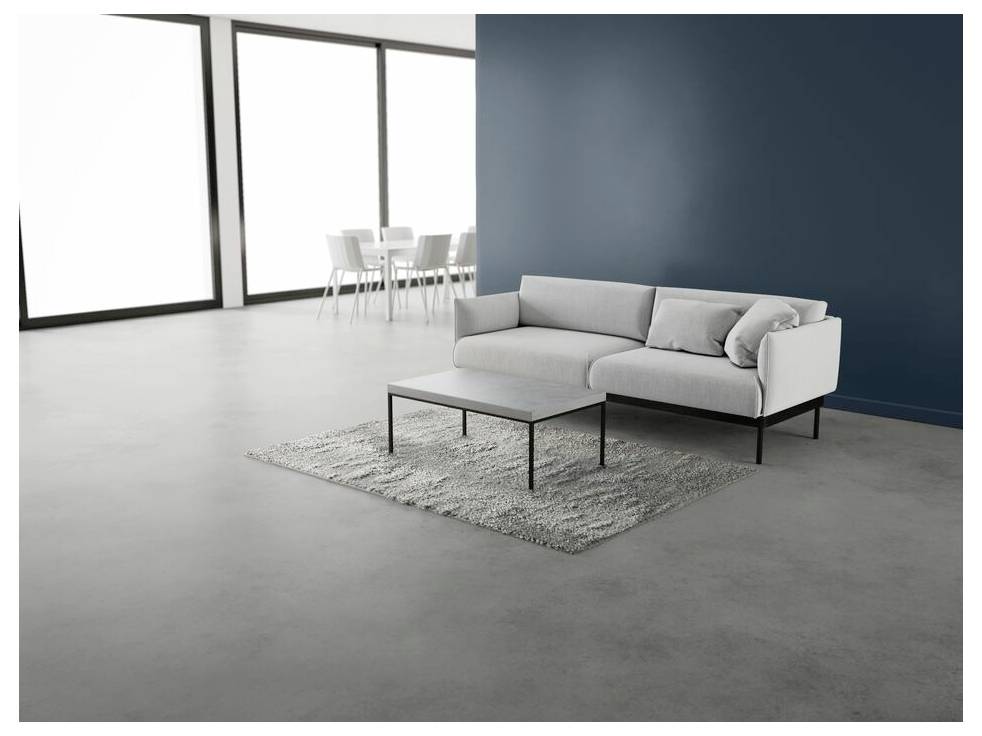 Ein modernes Wohnzimmer mit einem weißen Sofa vor einer dunkelblauén Wand, einem passenden Couchtisch auf einem hellgrauen Teppich und einem Essbereich im Hintergrund.