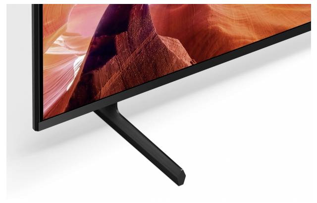 Nahaufnahme einer Ecke eines Flachbildfernsehers auf einem V-förmigen Ständer, auf dem ein lebhaft orangefarbenes Canyonbild auf dem Bildschirm angezeigt wird.
