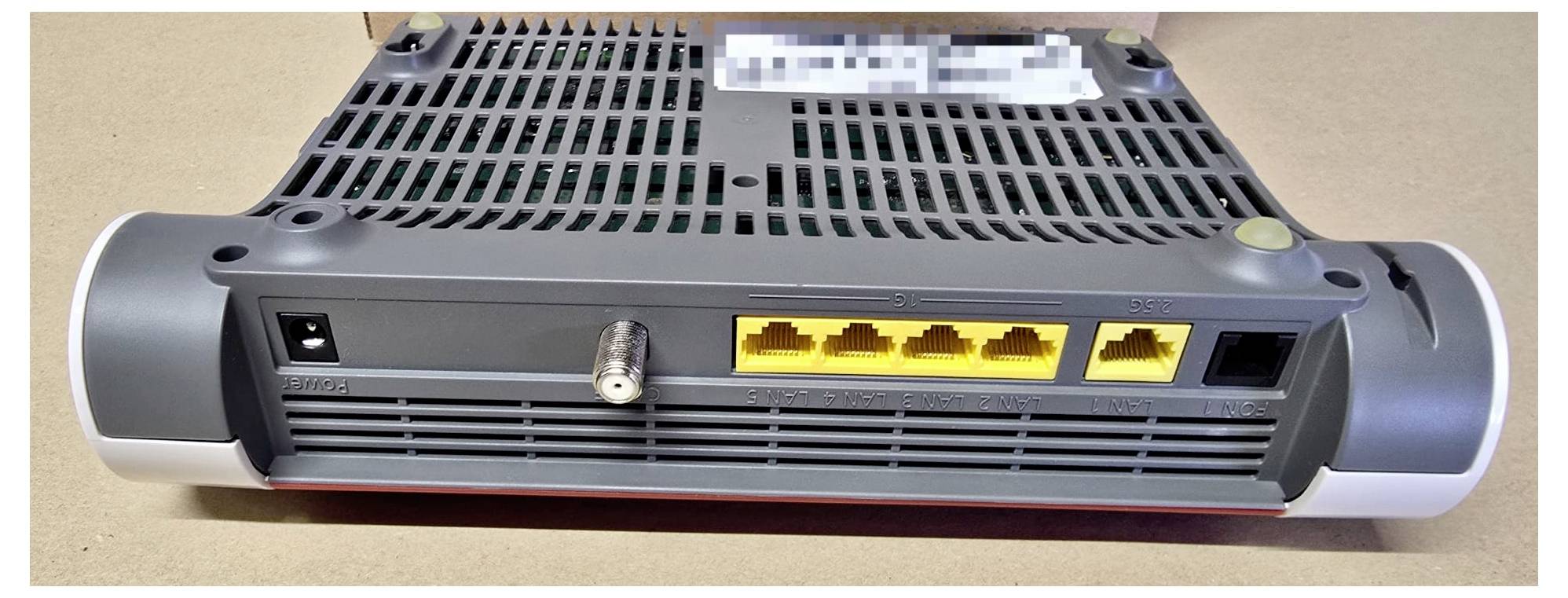 Rückansicht eines Routers, der vier gelbe Ethernet-Anschlüsse, einen Koaxialkabeleingang und eine Stromverbindung auf einer beigen Oberfläche zeigt.