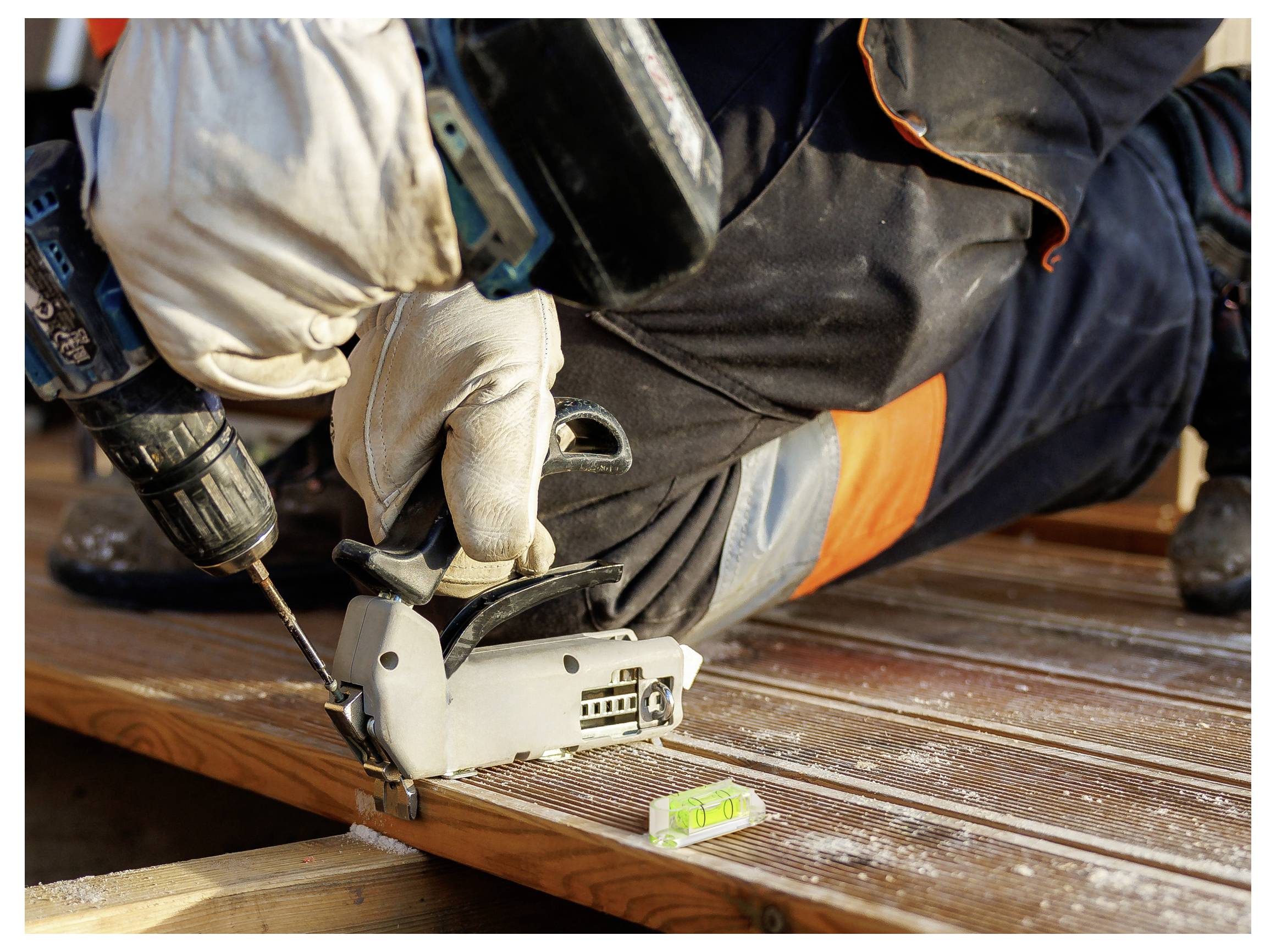 Handschuhgetragener Arbeiter, der einen Bohrer und eine Nagelmaschine verwendet, um ein Holzdeckenbrett zu befestigen, mit einem Stahllineal in der Nähe.