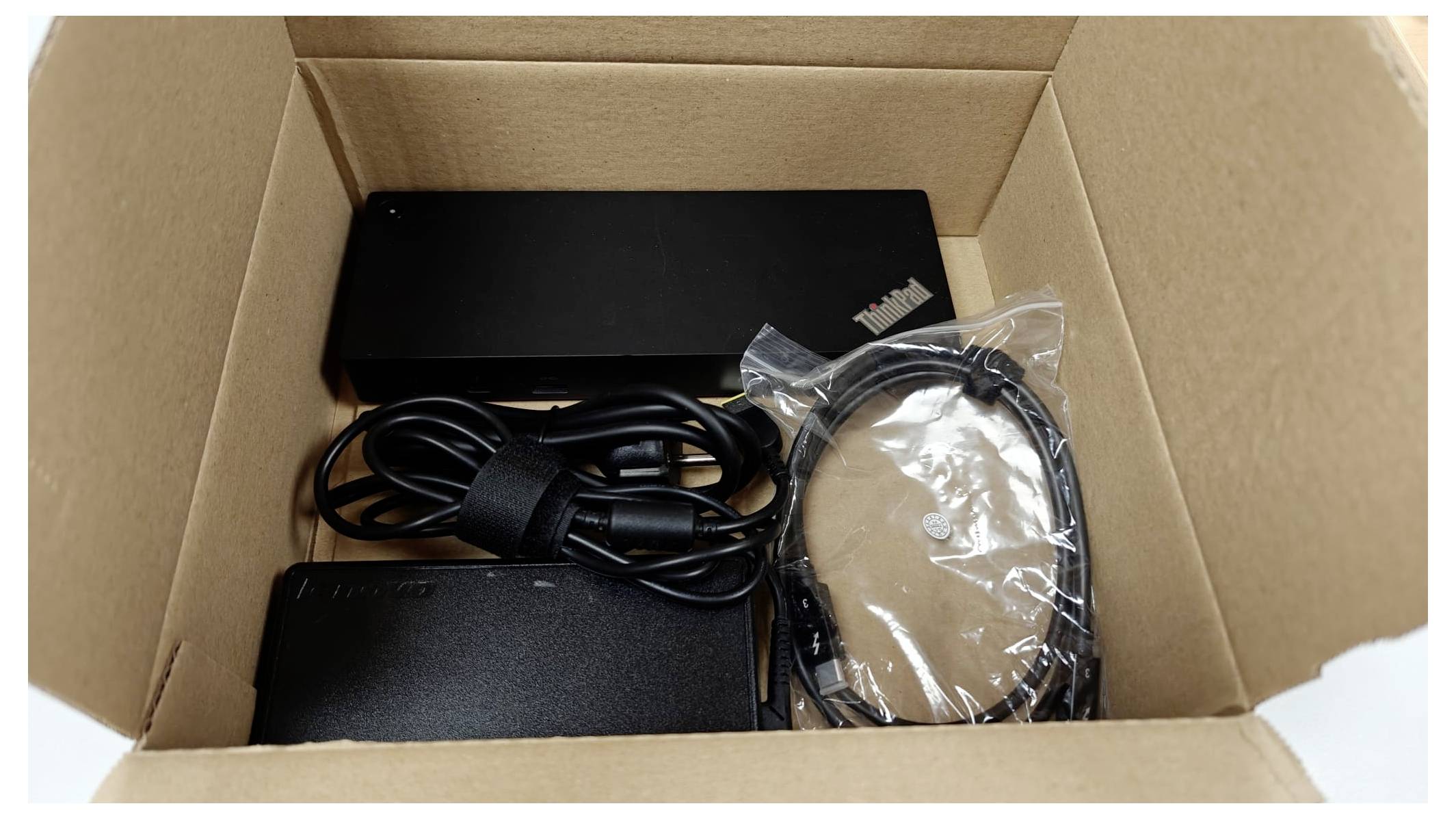 Eine Pappe schachtung enthält ein schwarzes elektronisches Gerät, einen Stromadapter und Kabel, die sauber für den Versand oder das Auspacken angeordnet sind.