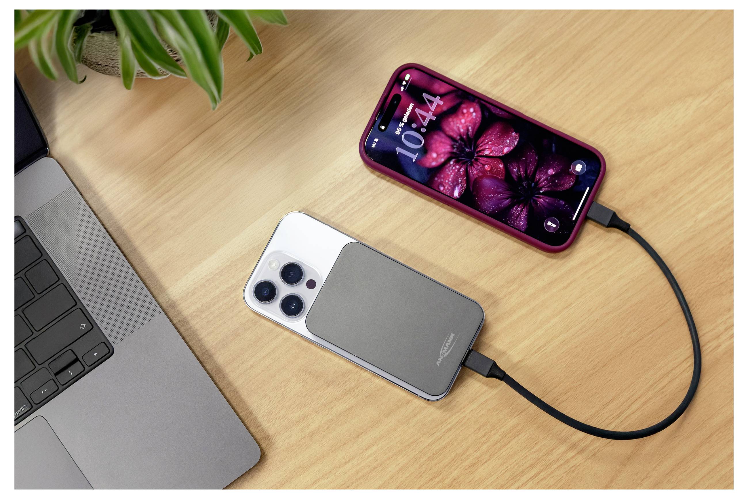 Drahtlose Ladesystem: Ein Smartphone und ein iPhone-ähnliches Telefon, die mit Kabeln auf einem Schreibtisch neben einem Laptop verbunden sind und mobiles Laden zeigen.