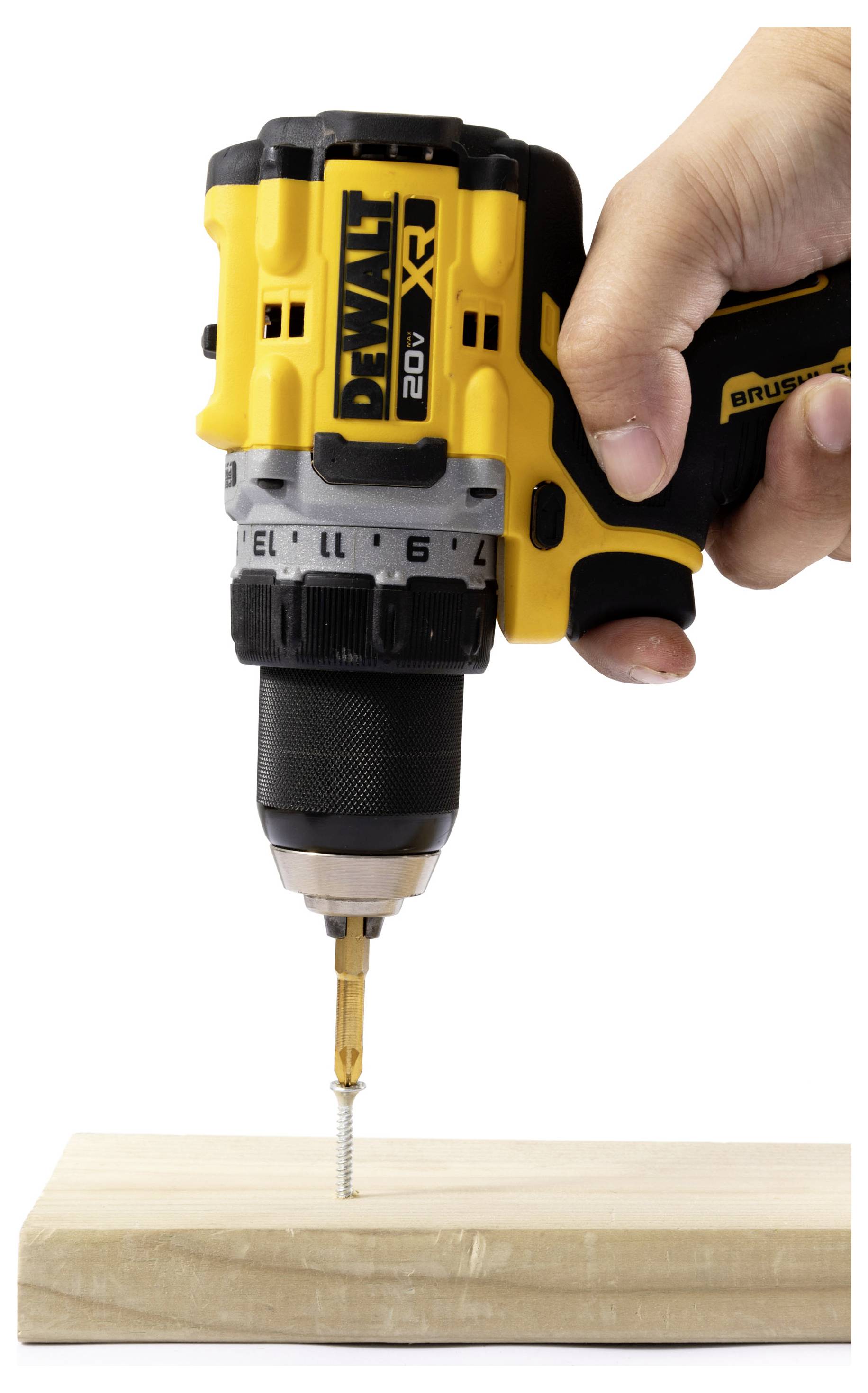 Eine Hand hält einen gelben DeWalt Akkubohrer und treibt eine Schraube in ein Holzbrett auf weißem Hintergrund ein.