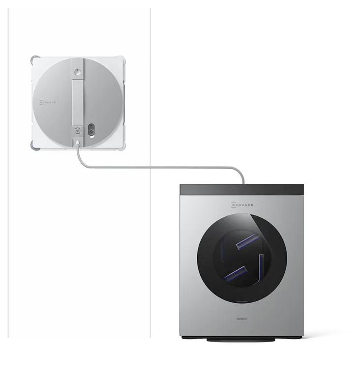 Das Bild zeigt einen silbernen Roboter-Fensterreiniger, der an einer Wand befestigt ist und über ein Kabel mit einer eigenständigen rechteckigen Einheit mit einem kreisförmigen Fenster verbunden ist.