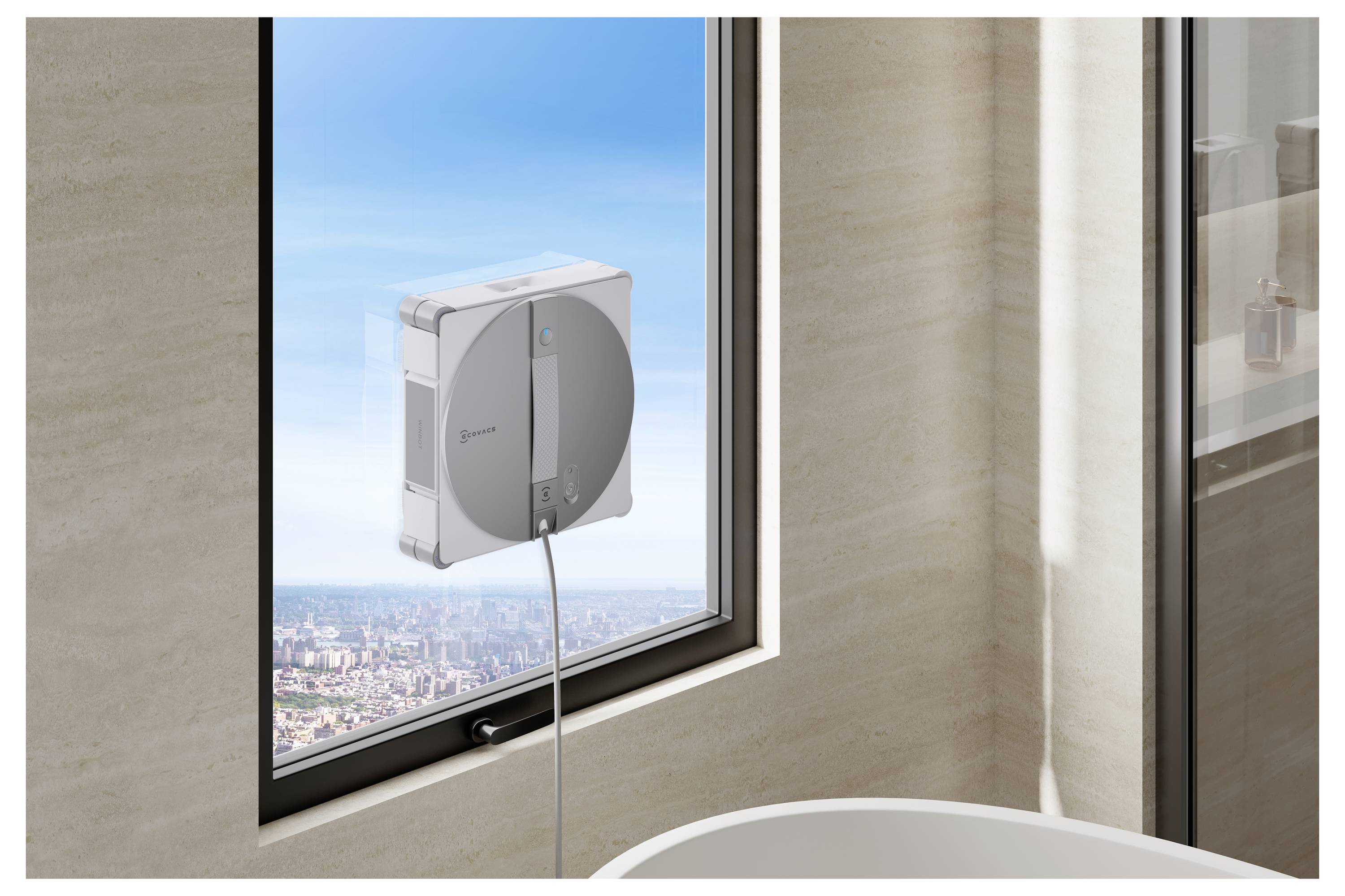 Ein Fensterputzroboter, der an einem Badezimmerfenster befestigt ist, mit Blick auf eine Stadtlandschaft außerhalb eines Hochhauses.