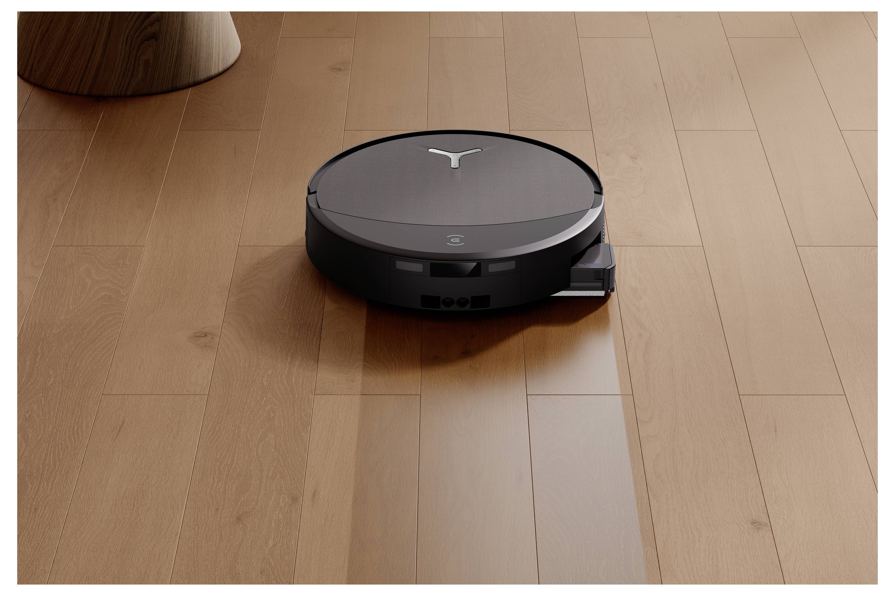 Ein runder Roboterstaubsauger auf Holzbodenbelag, der autonom neben einem Möbelbein navigiert.