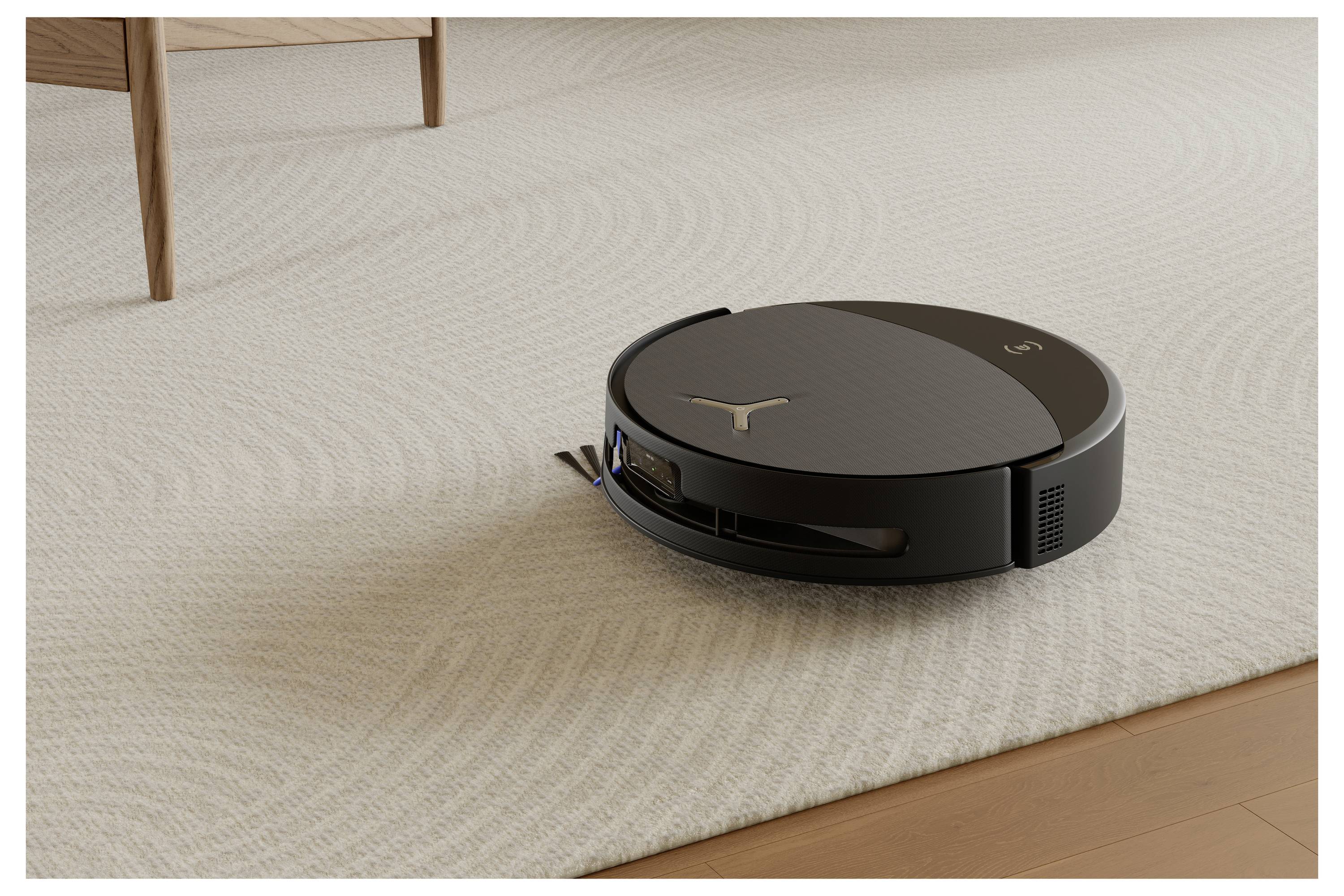 Ein schwarzer Roboterstaubsauger auf einem Teppich neben einem Möbelstück aus Holz. Er reinigt autonom in einer Wohnumgebung.