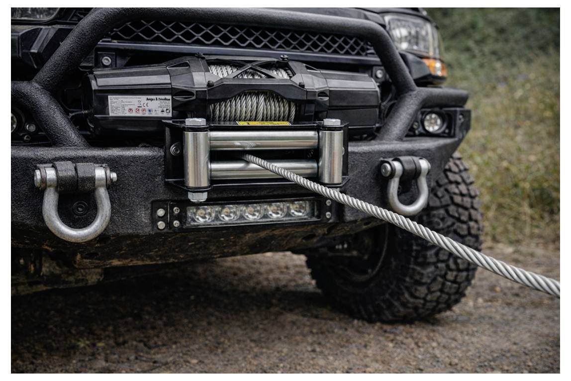 Nahaufnahme einer Geländewagen-Stoßstange mit einer montierten Winde und ausgefahrenem Stahlseil, bereit zur Bergung.