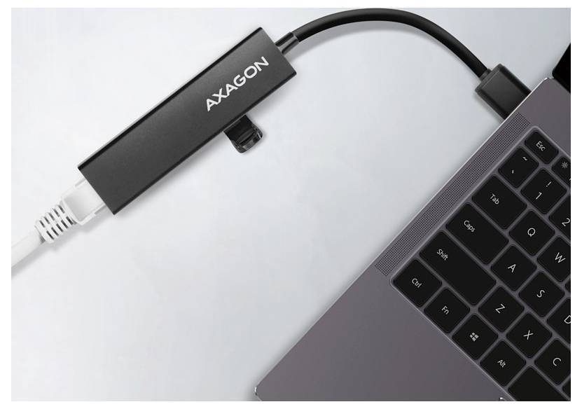 AXAGON USB-Adapter, der in einen Laptop eingesteckt ist, mit einem angeschlossenen Kabel, das sich von dem Gerät auf einer weißen Oberfläche erstreckt.