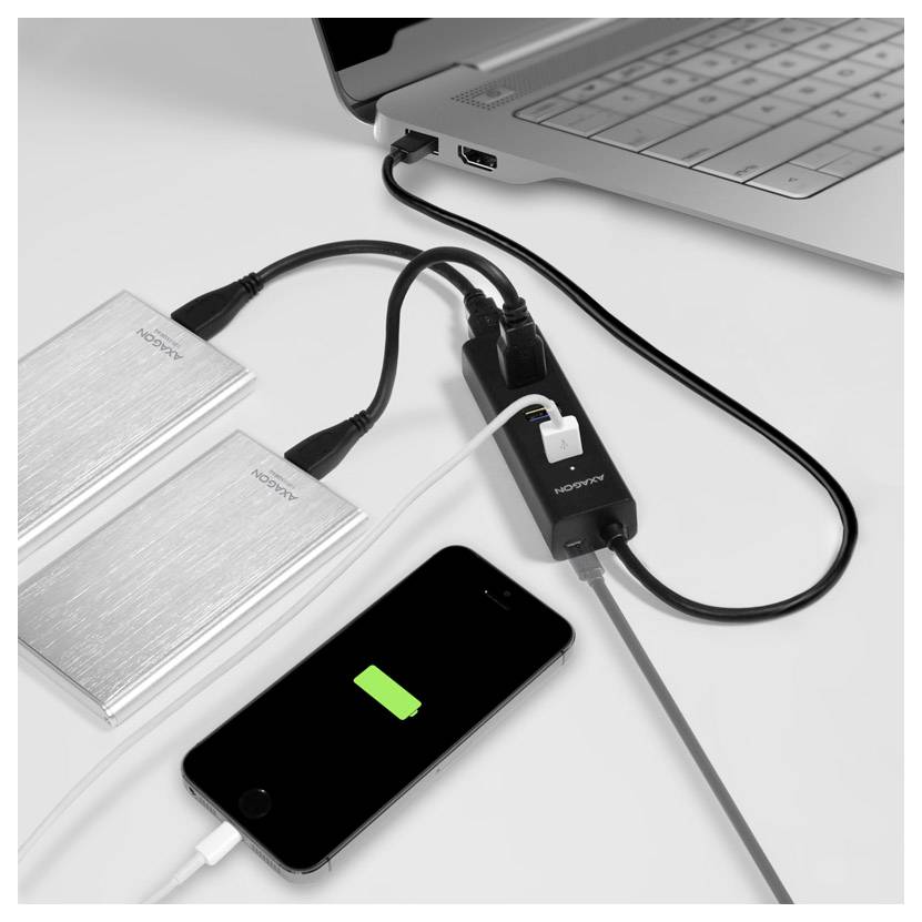 Laptop, der über einen USB-Hub auf einem weißen Schreibtisch mit zwei externen Festplatten verbunden ist und ein Smartphone lädt.
