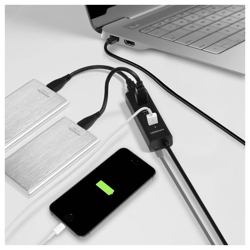 Laptop mit zwei externen Laufwerken und Smartphone-Laden über einen Multiport-Adapter auf einem Schreibtisch.