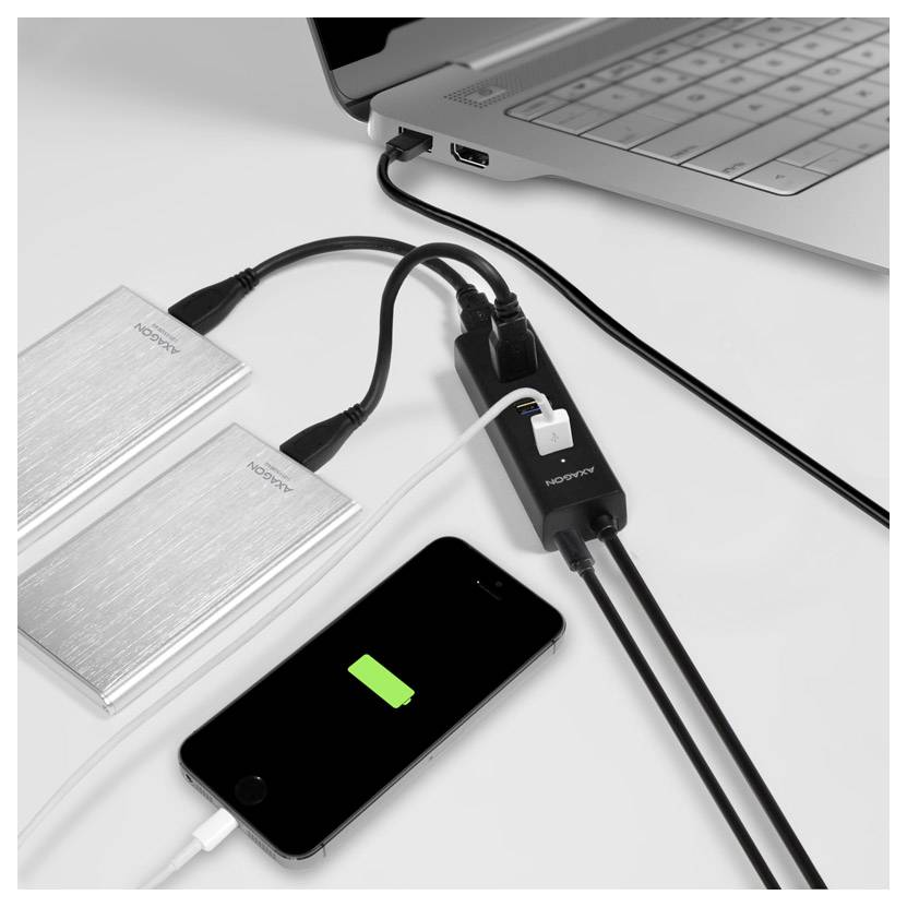 Ein Laptop versorgt zwei externe Festplatte mit Strom und lädt ein Smartphone über einen Multi-Port-Hub auf einem Schreibtisch auf.