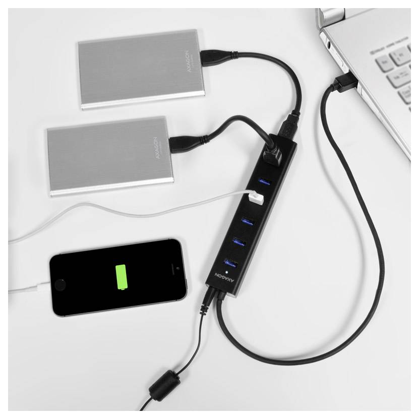 Zwei externe Festplatten und ein Smartphone sind mit einem USB-Hub neben einem Laptop verbunden, wobei das Telefon ein Ladesymbol mit Batterie anzeigt.