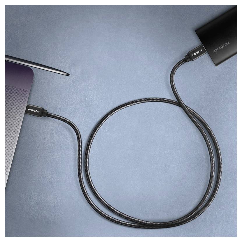 Laptop, der über ein schwarzes USB-C-Kabel mit einem externen Monitor oder einer Dockingstation auf einer blauen Oberfläche verbunden ist.