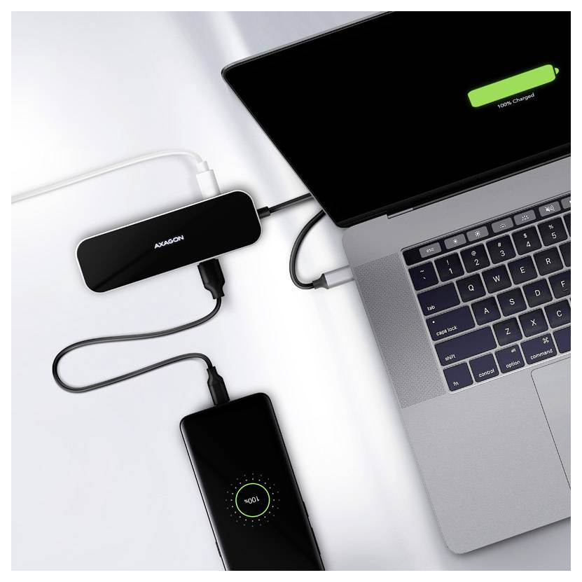 Laptop verbunden mit einem USB-C-Hub und Smartphone wird auf einem weißen Schreibtisch aufgeladen, wobei bei beiden Geräten der laufende Akkuladevorgang angezeigt wird.