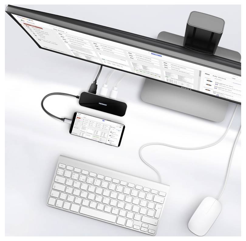 Draufsicht auf einen Desktop-Setup mit einem ultraleitenden Monitor, einer angedockten Smartphone, Tastatur, Maus und einem kleinen Hub, die durch Kabel verbunden sind.