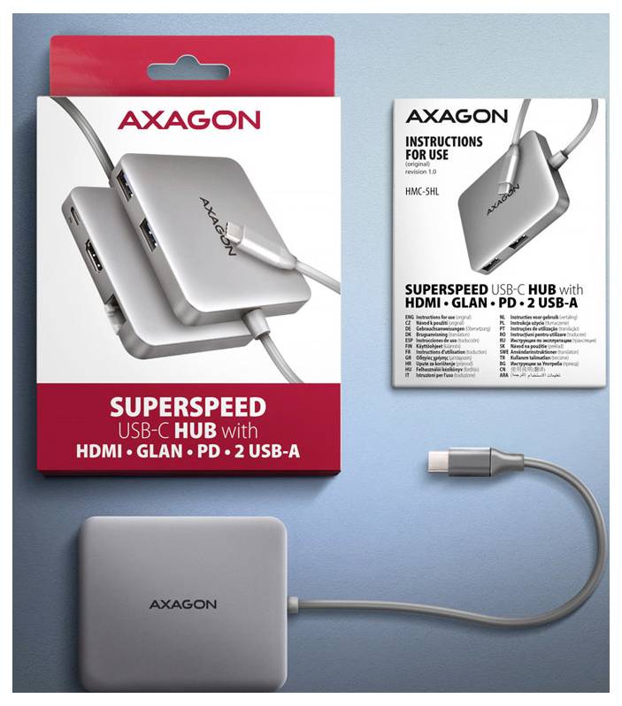 AXAGON SuperSpeed USB-C Hub Verpackung, Bedienungsanleitung und der silberfarbene Hub mit angeschlossenem Kabel und USB-C-Stecker auf blauem Hintergrund.