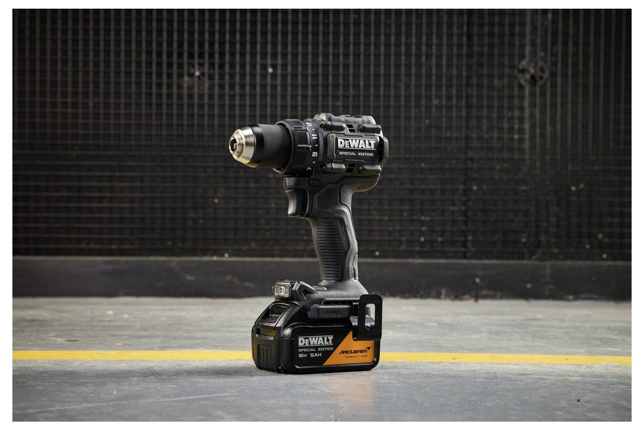 Schwarze DeWalt Akku-Bohrmaschine aufrecht auf ihrem Akku-Pack stehend vor einem dunklen Industriehintergrund mit gelber Bodenlinie.