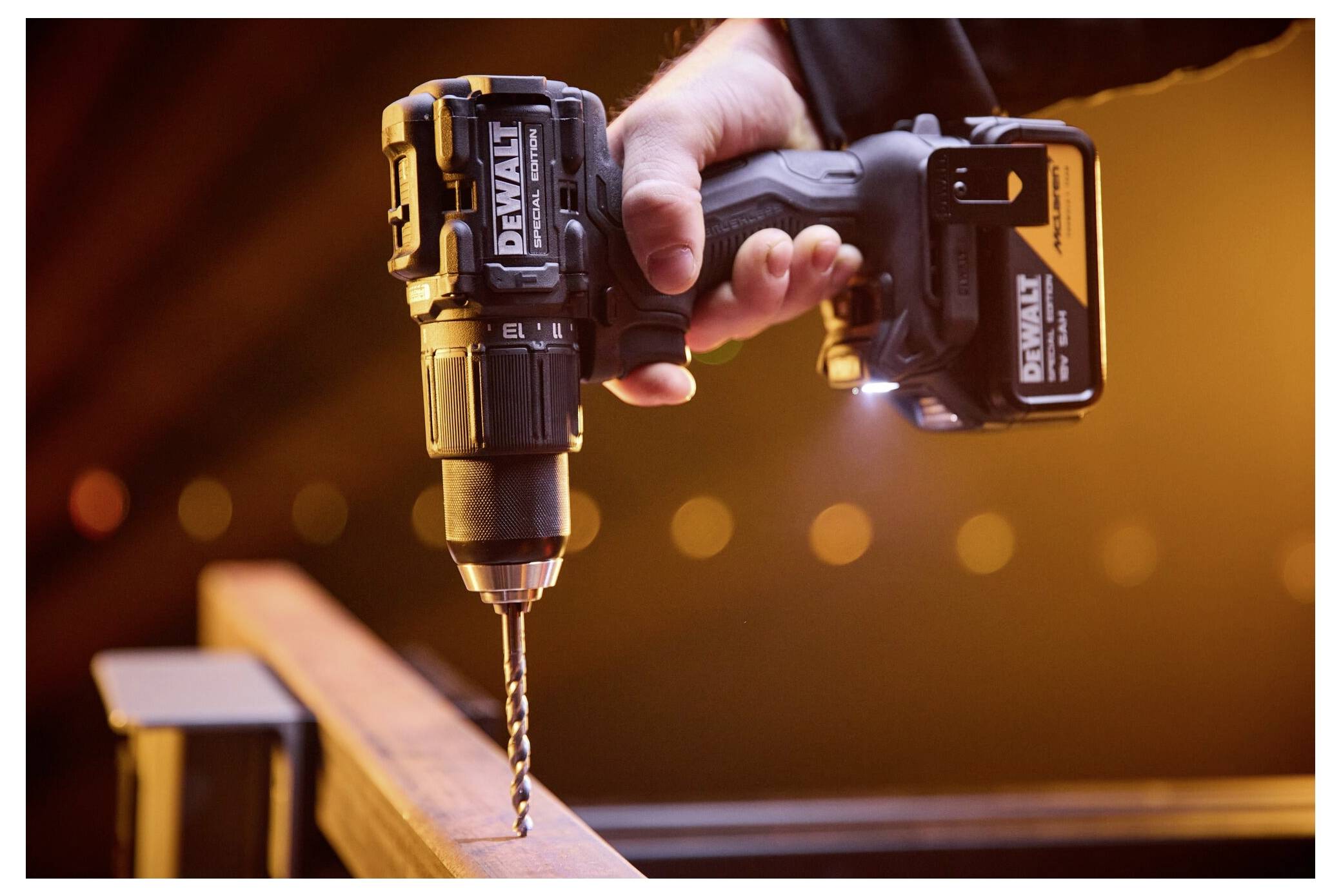 Eine Hand benutzt einen kabellosen Bohrer, um ein Loch in ein Holzbrett zu bohren, wobei der Bohrer in Großaufnahme beleuchtet ist.
