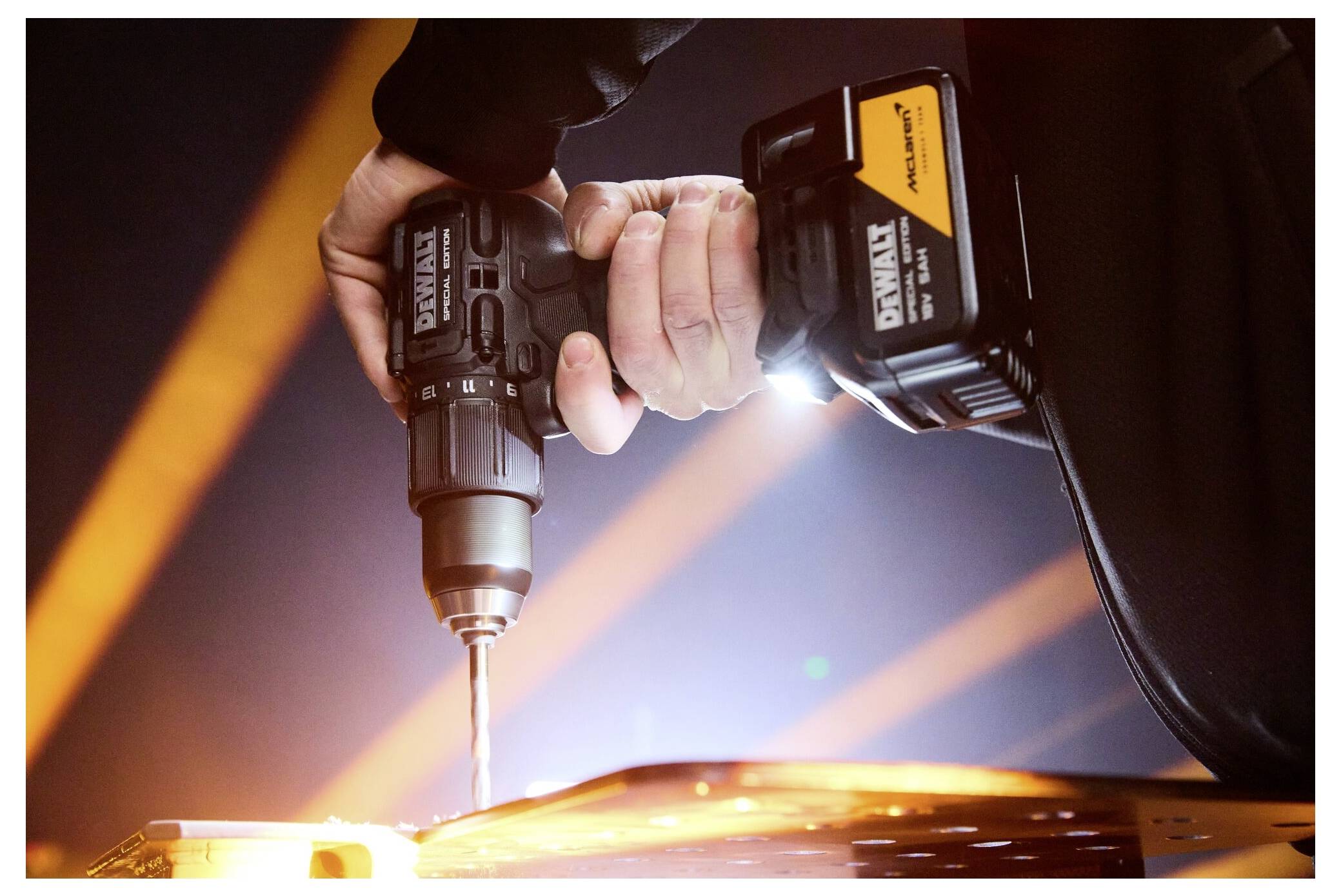 Nahaufnahme einer Person, die einen schnurlosen Elektroschrauber verwendet, um in eine glühende Metalloberfläche zu bohren, wobei helle Funken und orangefarbenes Licht entstehen.