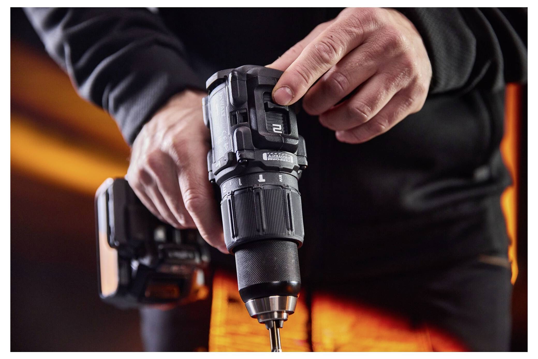 Person, die einen kabellosen Bohrer verwendet, einen Bohraufsatz hält und festzieht, mit einem angebrachten Akku und orangefarbener Arbeitskleidung im Hintergrund.