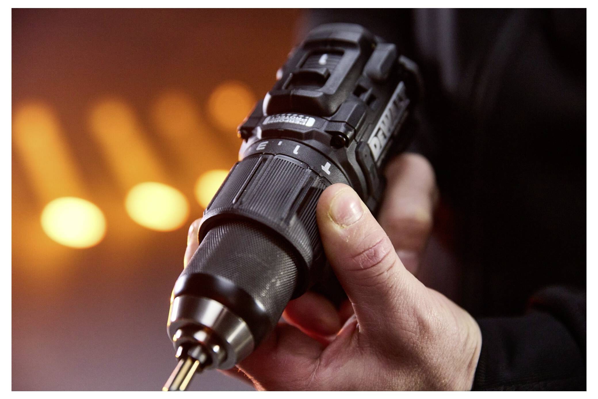 Nahaufnahme einer Person, die einen Akkubohrer hält, mit unscharfem, warmem orangefarbenem Hintergrund.