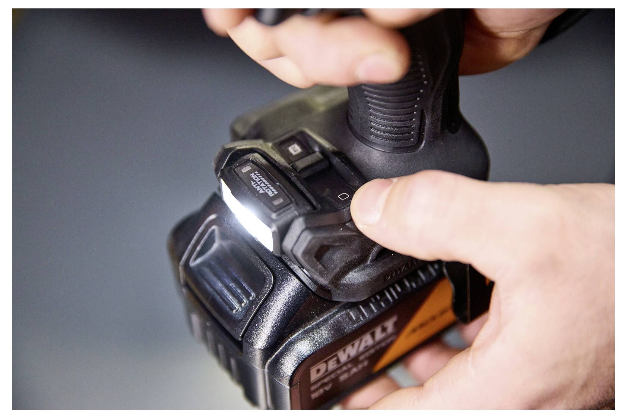 Nahaufnahme von Händen, die eine Taste auf einem DeWalt-Akku für kabellose Bohrmaschinen drücken, mit dem sichtbaren Bohrmaschinen­griff.