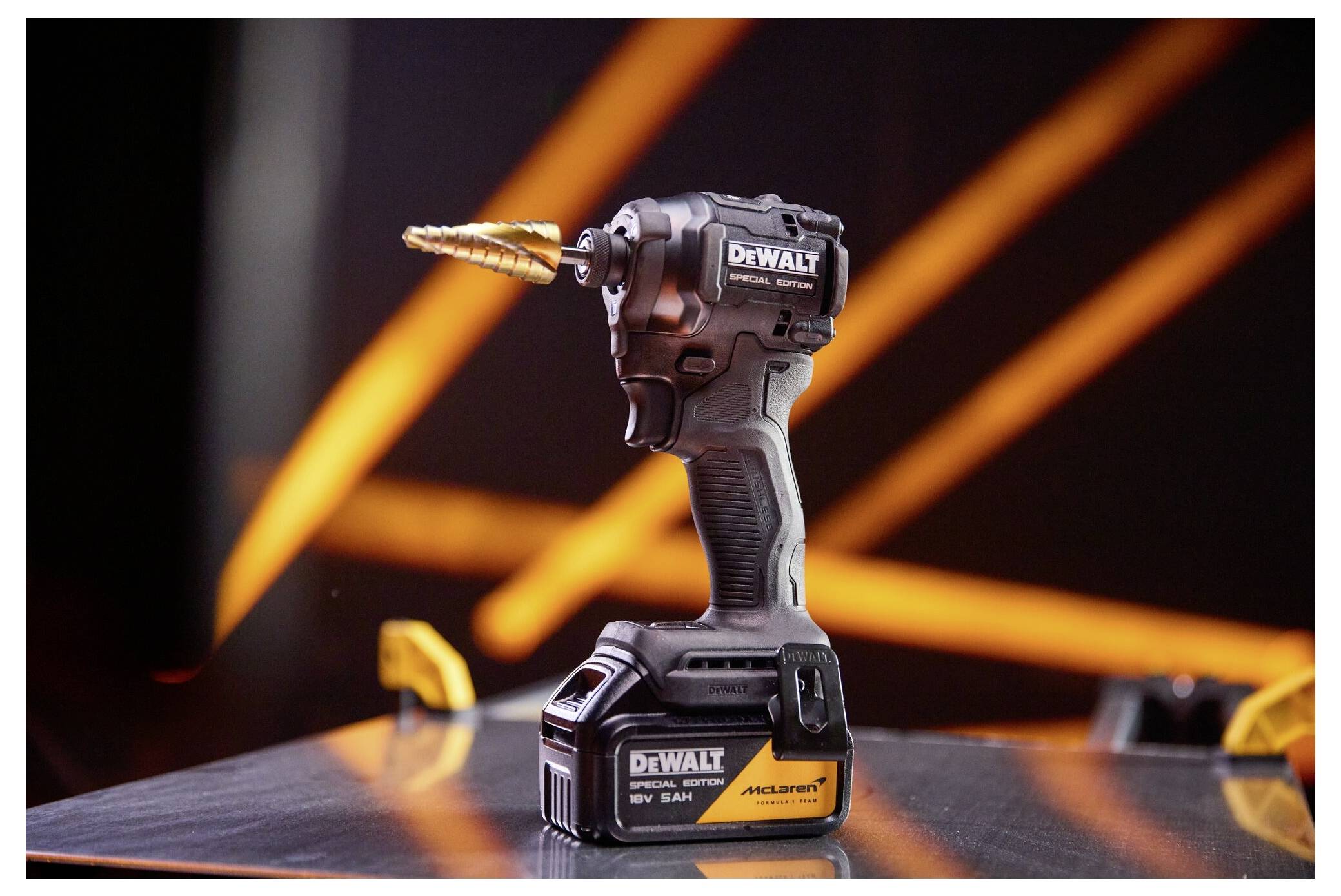 Eine DeWalt-Akku-Bohrmaschine mit einem Goldaufsatz steht auf einer reflektierenden Oberfläche, mit orangefarbenen Lichtstreifen im Hintergrund.