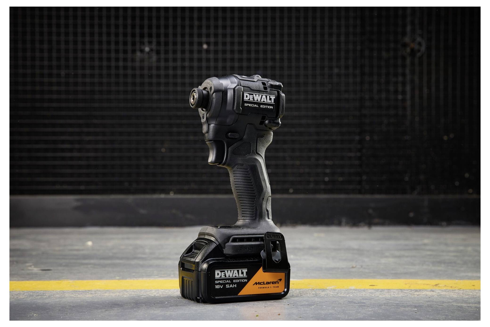 Schwarzer DeWalt Akku-Schlagschrauber, aufrecht auf einem Betonboden mit einer gelben Linie stehend, vor einem dunklen Industriehintergrund.