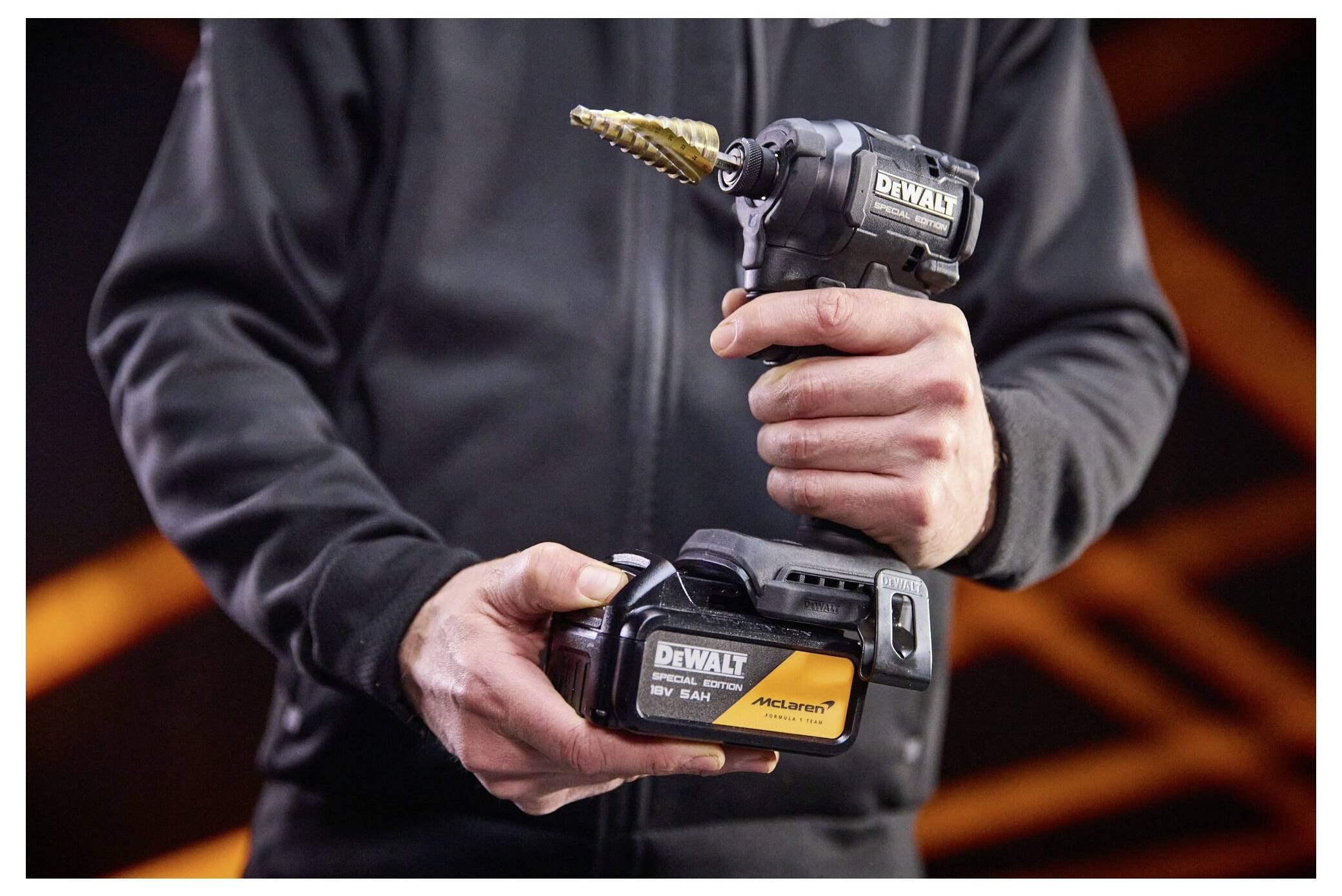 Person holding a DEWALT cordless right-angle drill with a step bit and matching battery pack.Person, der einen DEWALT Akku-Winkelbohrer mit einem Stufenbohrer und passendem Akkupack hält.