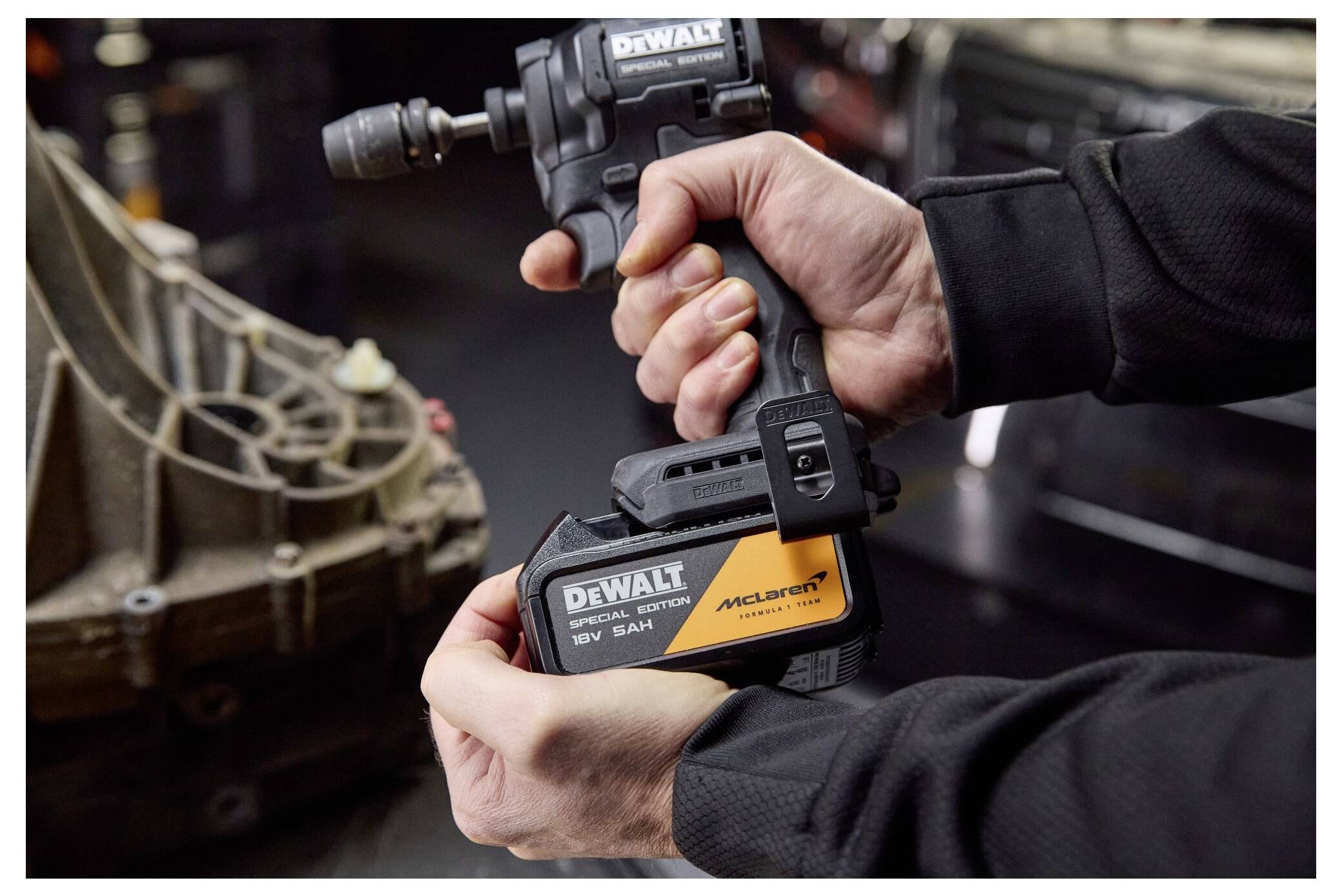 Nahaufnahme von Händen, die einen DeWalt 18V Akku-Schlagschrauber mit McLaren-Akku verwenden, um ein Fahrzeugteil in einer Werkstatt festzuziehen oder zu lockern.