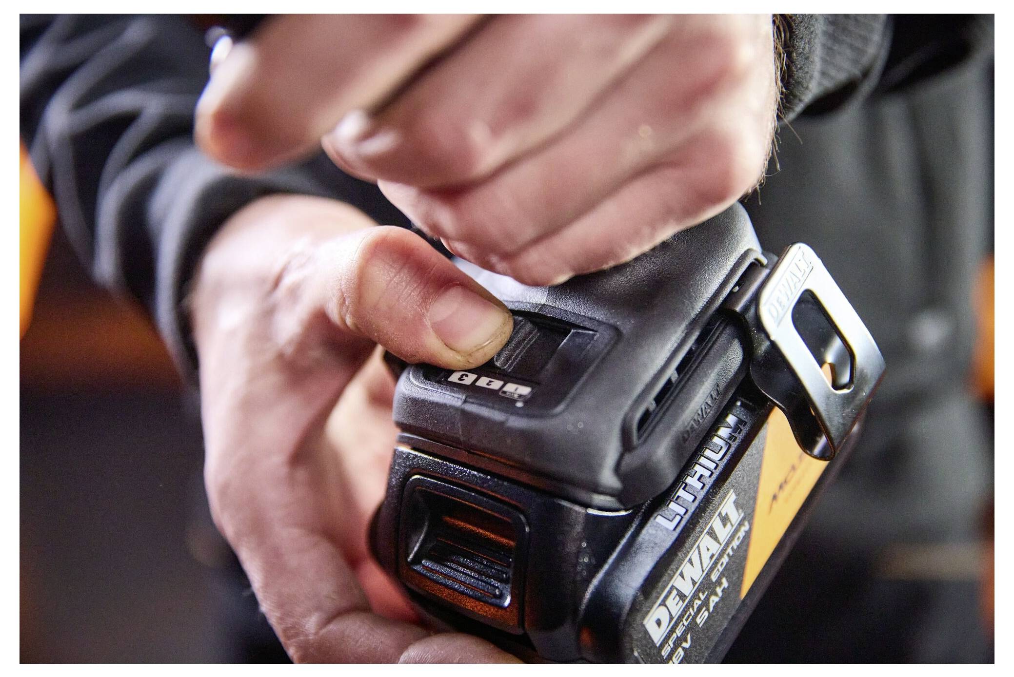 Nahaufnahme einer Hand, die den Auslöseknopf an einem DeWalt-Akkupack anpasst, der an einem Elektrowerkzeug befestigt ist.