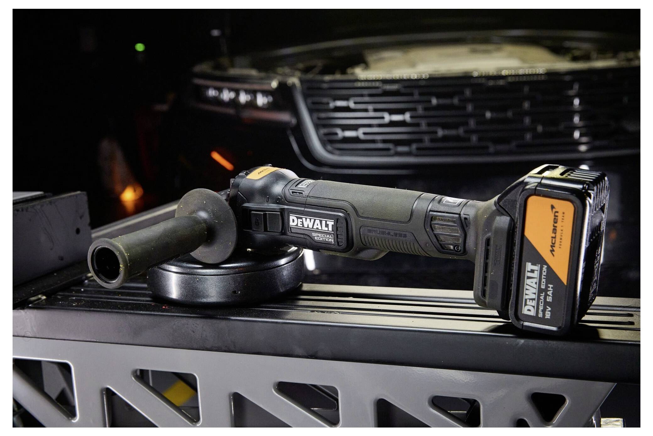 Ein DEWALT kabelloses Winkelschleifer mit Akku ruht auf einer Metalloberfläche vor einem Fahzeuggrill.