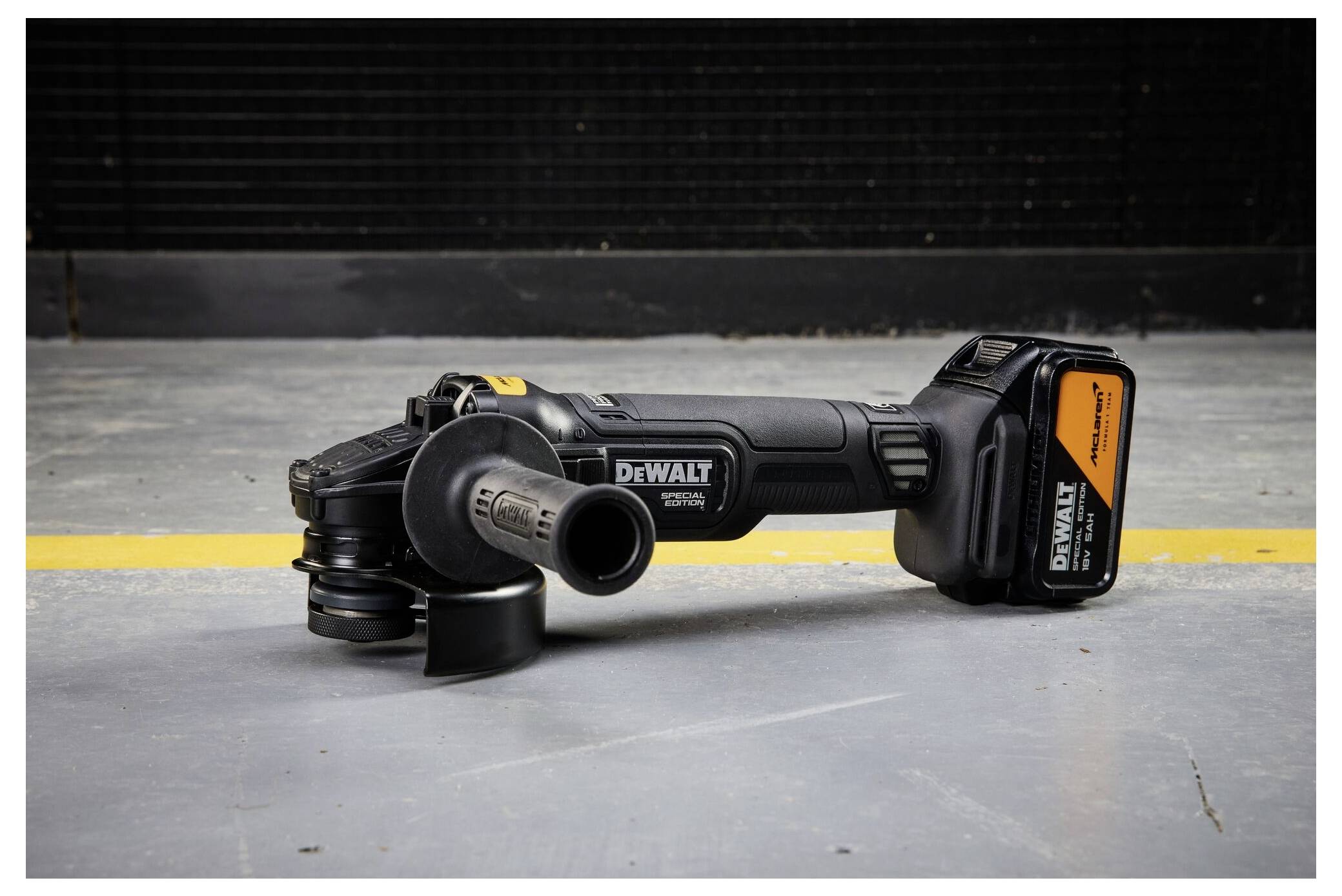 Ein kabelloses Winkelschleifer-Modell von DeWalt liegt auf einem Betonboden in einer Werkstatt, dargestellt in einer Seitenansicht mit der angebrachten Batterie.