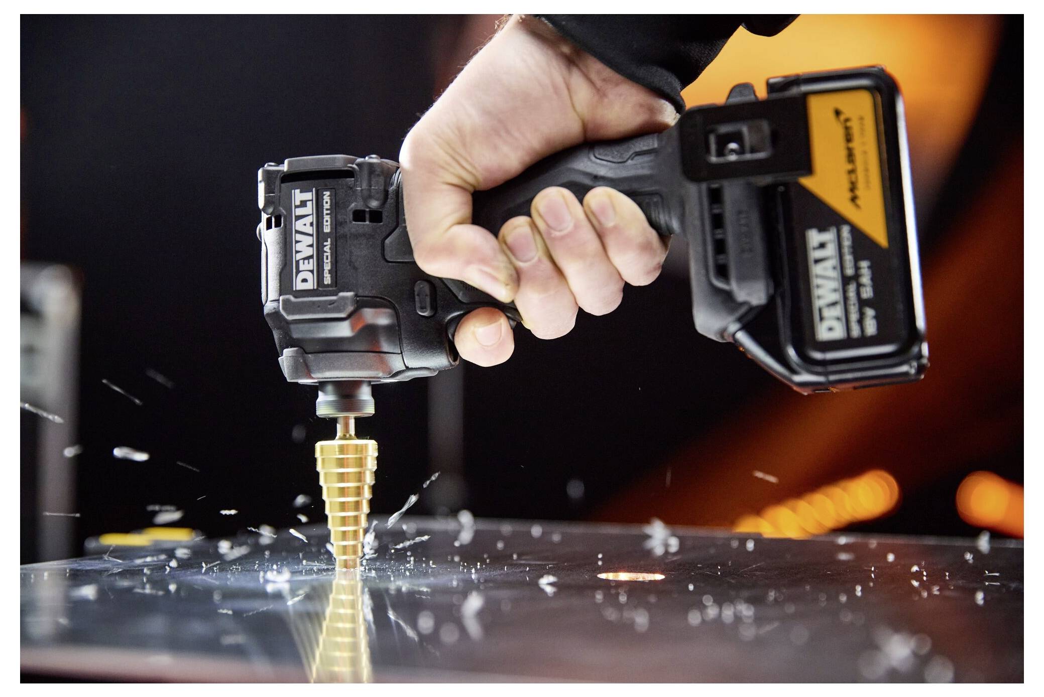 Nahaufnahme einer Person, die einen kabellosen DeWalt-Bohrer mit einem Kegelbohrer verwendet, um durch Metall zu bohren, wobei Funken fliegen.