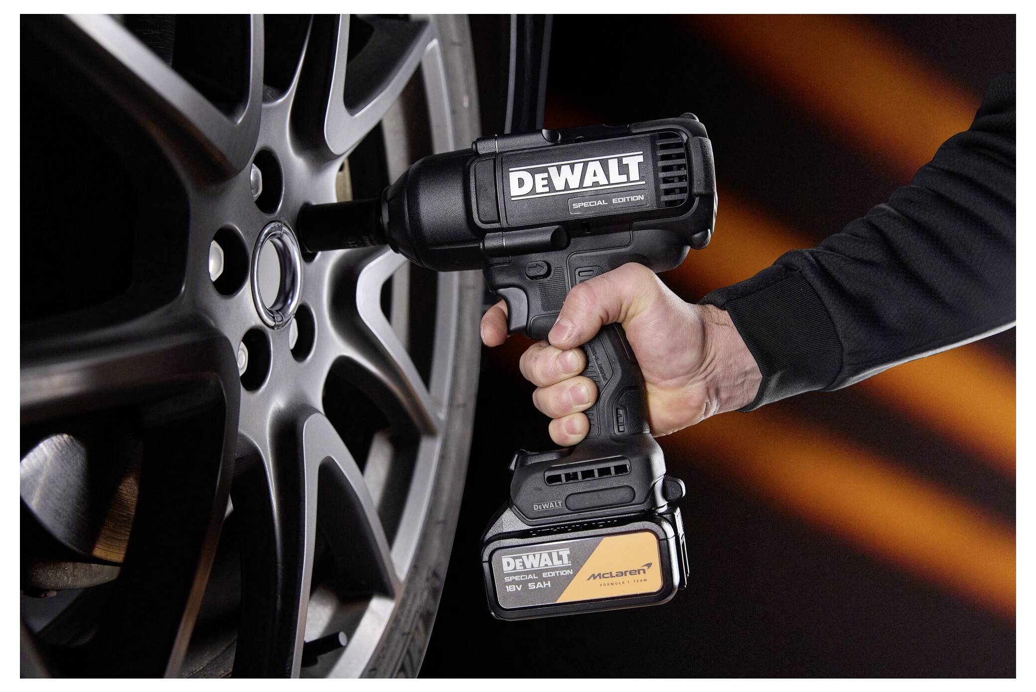 Hand hält einen DEWALT Akku-Schlagschrauber fest, der eine Radmutter an einem silbernen Leichtmetallrad anspannt.