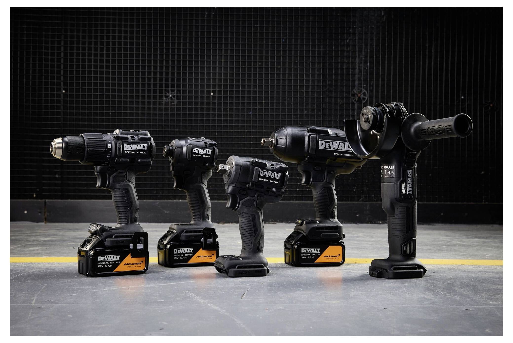 Vier kabellose DeWalt-Elektrowerkzeuge auf einem Betonboden: drei Bohrschrauber und ein kompaktes Werkzeug, wobei der rechts liegende Bohrschrauber mit einem Aufsatz ausgestattet ist.
