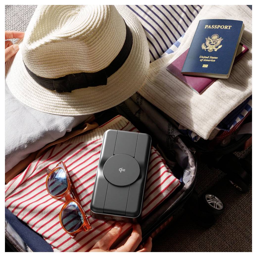 Gepackte Reiseartikel in einem Koffer: Strohhut, US-Pass, zusammengefaltete Kleidung, Sonnenbrille und ein tragbares Ladegerät, was auf Reisevorbereitung hindeutet.