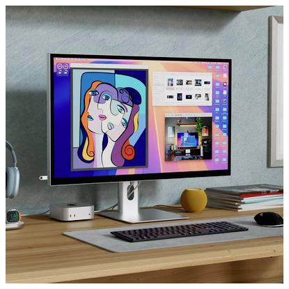 Ein Desktopmonitor zeigt ein farbenfohes Kunstbild an, und zwei offene Fenster sind auf einem ordentlich aufgeräumten Schreibtisch im Homeoffice zu sehen, zusammen mit Tastatur, Maus, Lautsprecher und gestapelten Büchern.