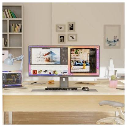 Ein modernes Schreibtisch-Setup mit einem großen Monitor, auf dem Designsoftware angezeigt wird, einem Laptop, einer Tastatur, einer Maus und einer Lampe in einem hellen Homeoffice.