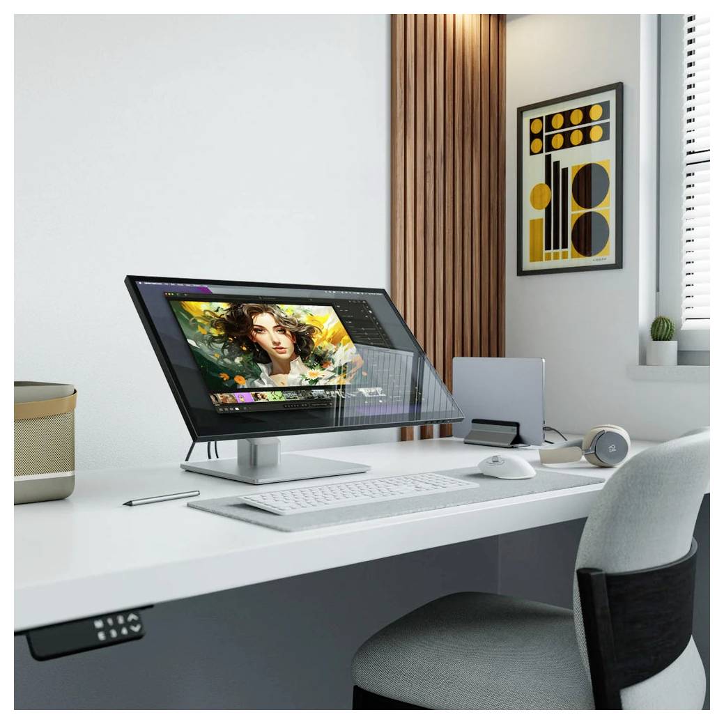 Moderner Schreibtisch-Arbeitsplatz mit großem Monitor, der digitale Kunstbearbeitung anzeigt, Tastatur, Maus, Kopfhörer und minimalistische Wandkunst in einem hellen Raum.