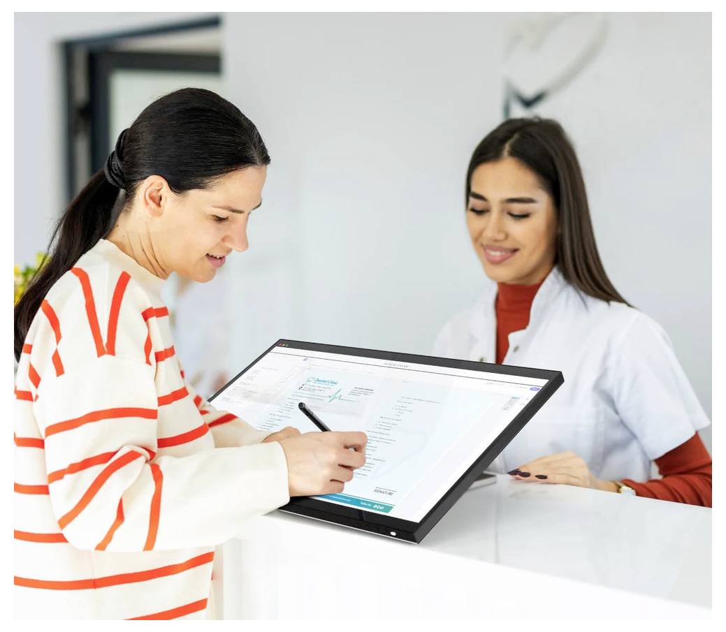 Eine Frau unterzeichnet ein Dokument auf einem digitalen Tablet, während eine lächelnde Empfangsdame im weißen Kittel an einem Serviceschalter Hilfe leistet.