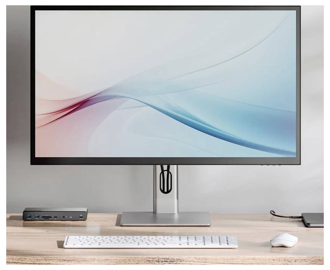 Modernes Schreibtischset mit einem Breitbildmonitor, Tastatur, Maus und einem kleinen Dock auf einem Holzschreibtisch vor einer schlichten Wand.