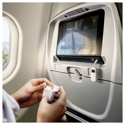 Passagier, der kabellose Ohrhörer in der Hand hält, während er in einem Flugzeug sitzt; Sitzlehnen-Display und Ladekabel sind sichtbar.
