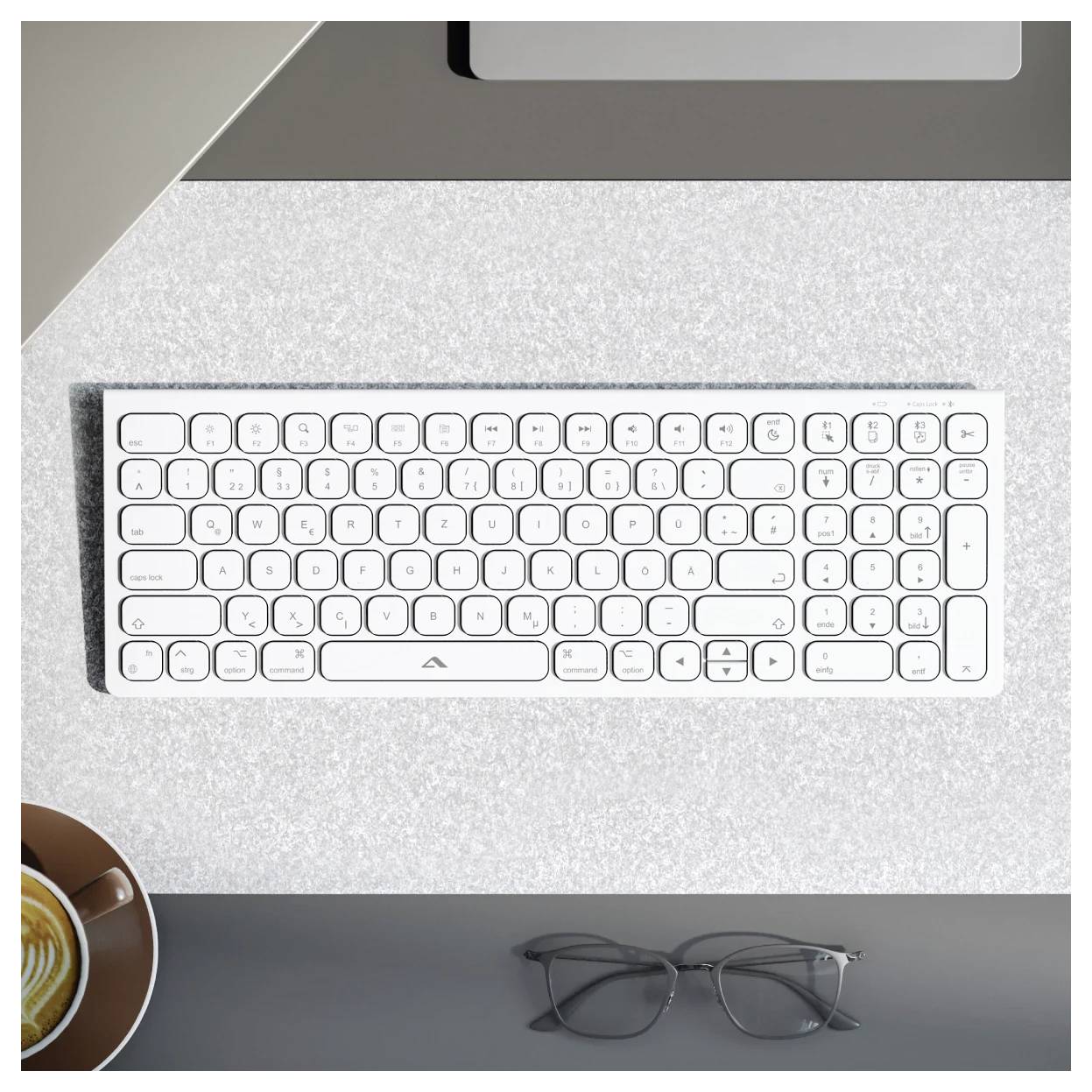 Draufsicht auf eine weiße schnurlose Tastatur auf einem hellen Schreibtisch, mit einer Kaffeetasse unten links und einer Brille unten rechts.