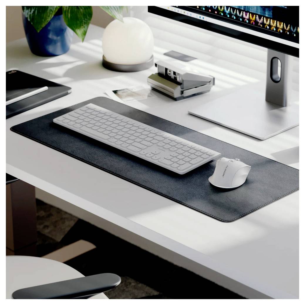 Minimalistisches weißes Schreibtisch-Setup mit Tastatur, Maus, Monitor und Lampe auf einer großen Schreibunterlage in einem modernen Arbeitsbereich.
