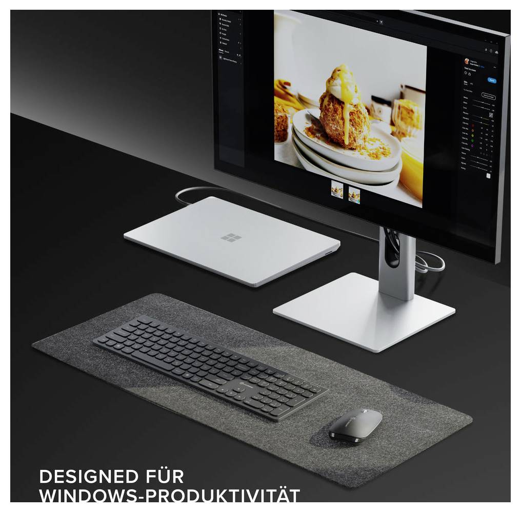 Arbeitsbereich mit Monitor, Tastatur, Maus und Surface-Zubehör; der Bildschirm zeigt Fotobearbeitung mit dem Text „ENTWORFEN FÜR WINDOWS-PRODUKTIVITÄT