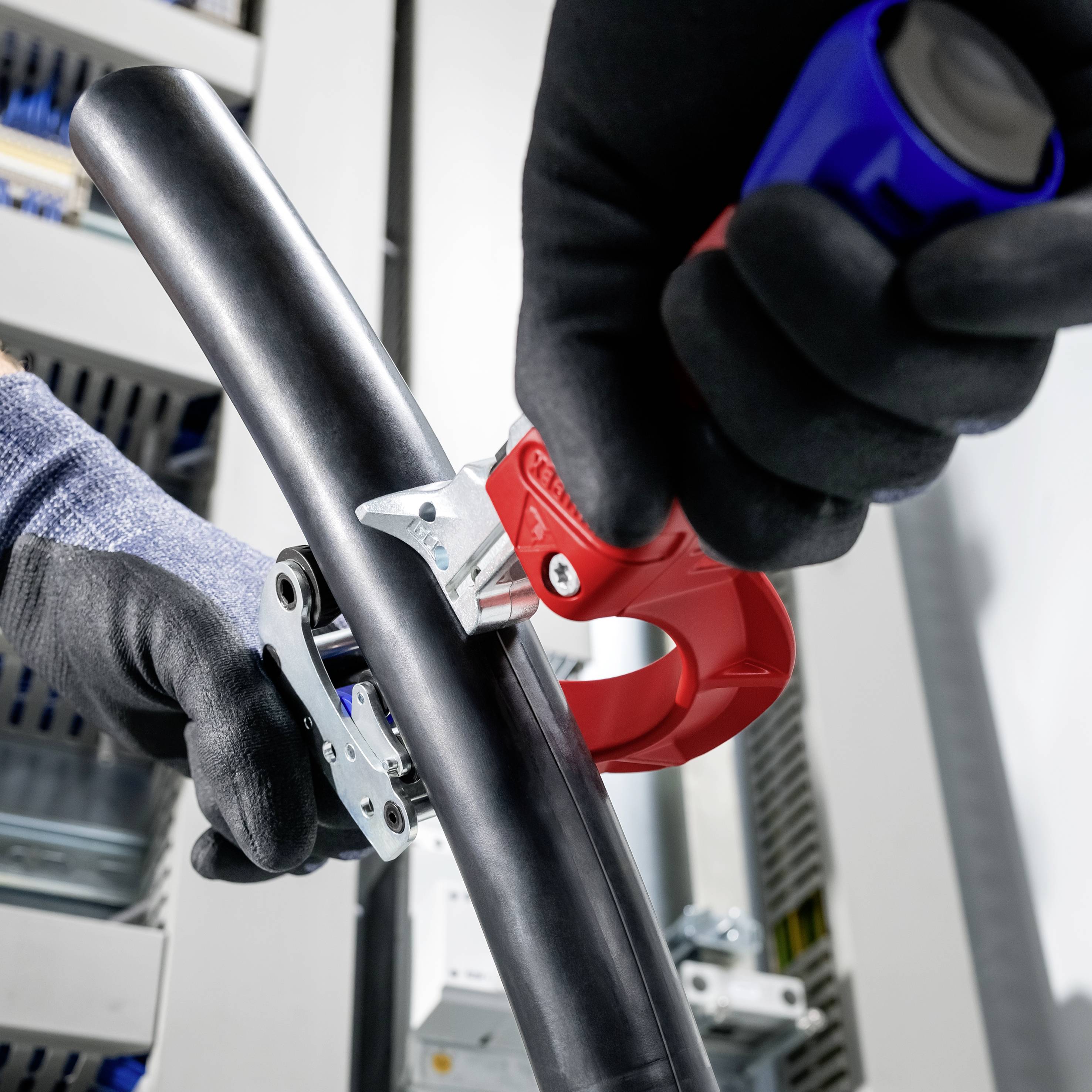 Behandschuhte Hände verwenden ein rotes Spannwerkzeug, um einen schwarzen Schlauch oder ein schwarzes Kabel an einer Maschine in einer industriellen Umgebung anzubringen.