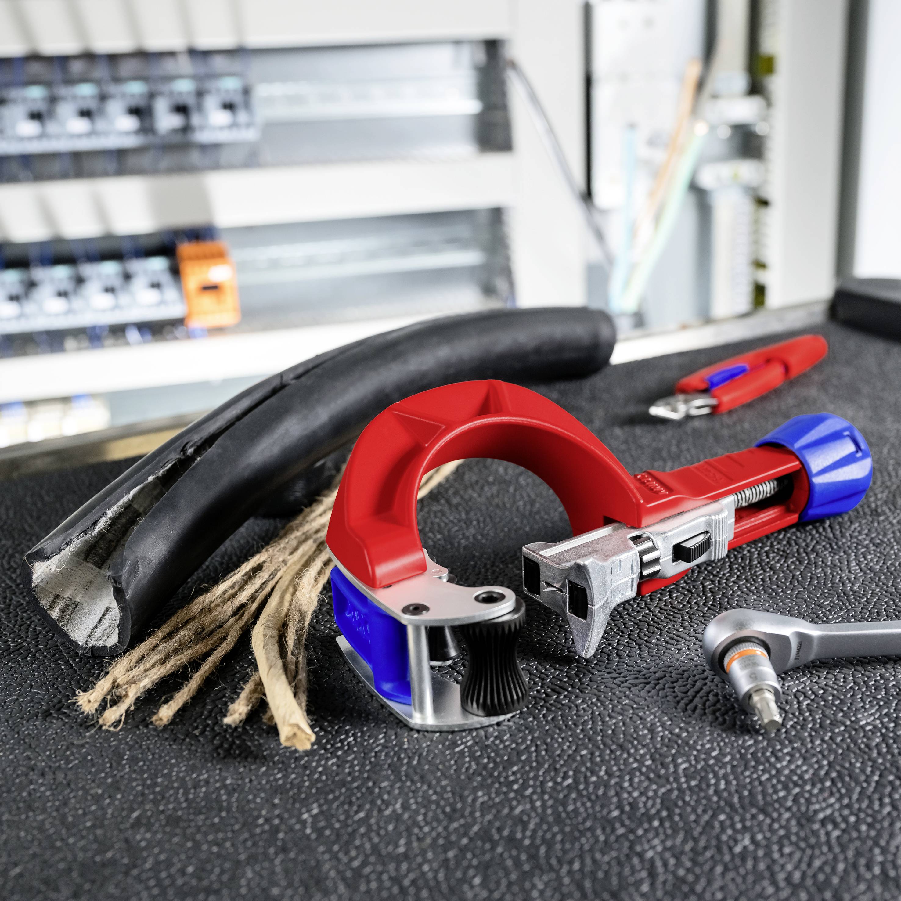 Kabelschneidewerkzeuge und ein abgestreiftes schwarzes Kabel, die auf einer Werkbank liegen, mit einem rot-blauen Schneider und Abisolierer in einer Werkstatt.
